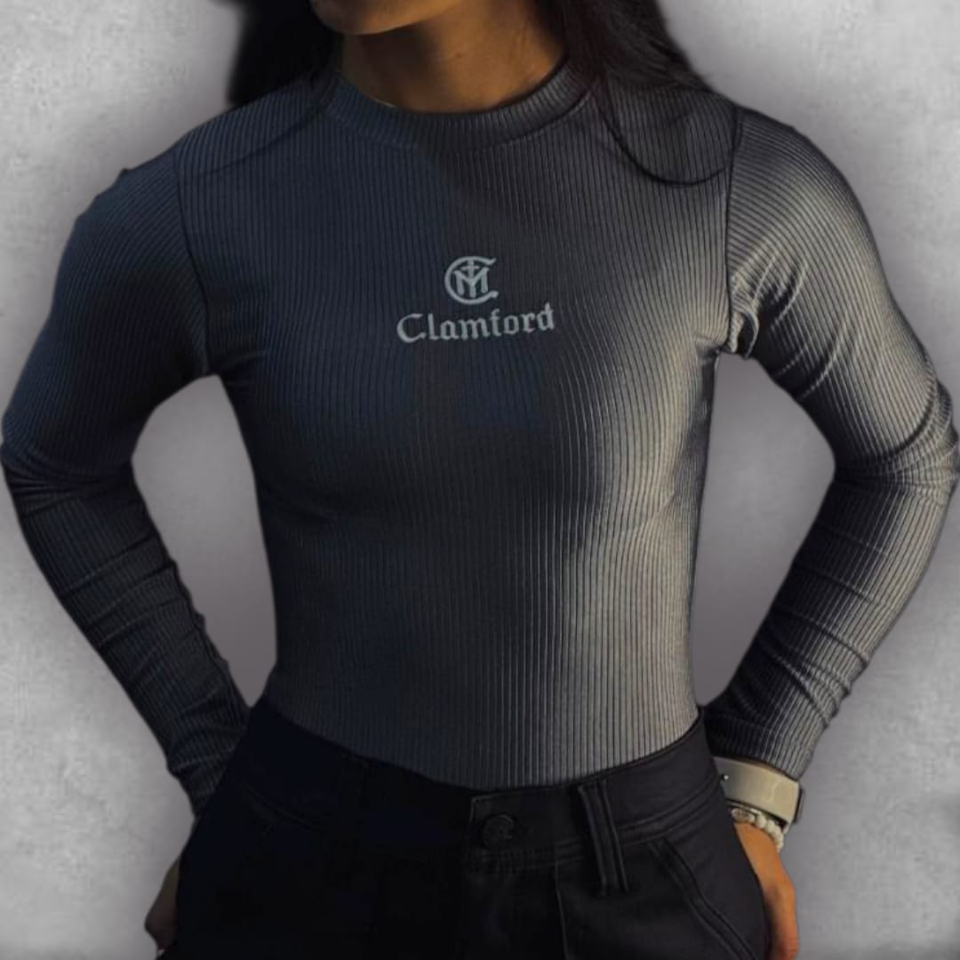 Atrévete con el color grafito del Body Clamford – Graphite Ribbed Edition. Su tejido elástico acanalado no solo garantiza un confort excepcional, sino que proporciona una textura rica que eleva su apariencia. El diseño de manga larga y cuello alto es un clásico reinventado para la moda contemporánea. El bordado frontal del logo de Clamford sella la prenda con un aire pulido y atemporal. Es la pieza imprescindible para lograr un estilo chic y versátil, ideal para cualquier ocasión.