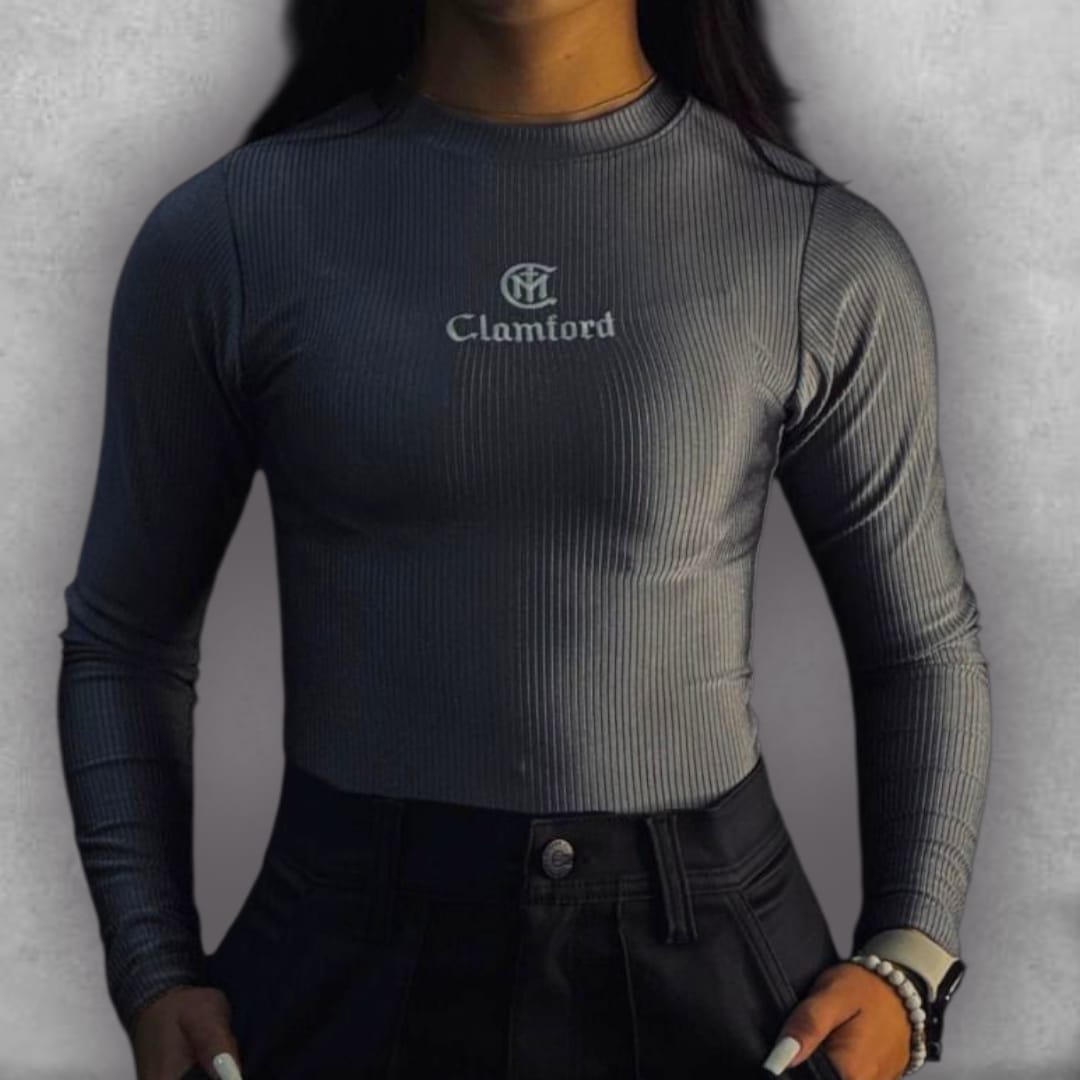 Atrévete con el color grafito del Body Clamford – Graphite Ribbed Edition. Su tejido elástico acanalado no solo garantiza un confort excepcional, sino que proporciona una textura rica que eleva su apariencia. El diseño de manga larga y cuello alto es un clásico reinventado para la moda contemporánea. El bordado frontal del logo de Clamford sella la prenda con un aire pulido y atemporal. Es la pieza imprescindible para lograr un estilo chic y versátil, ideal para cualquier ocasión.