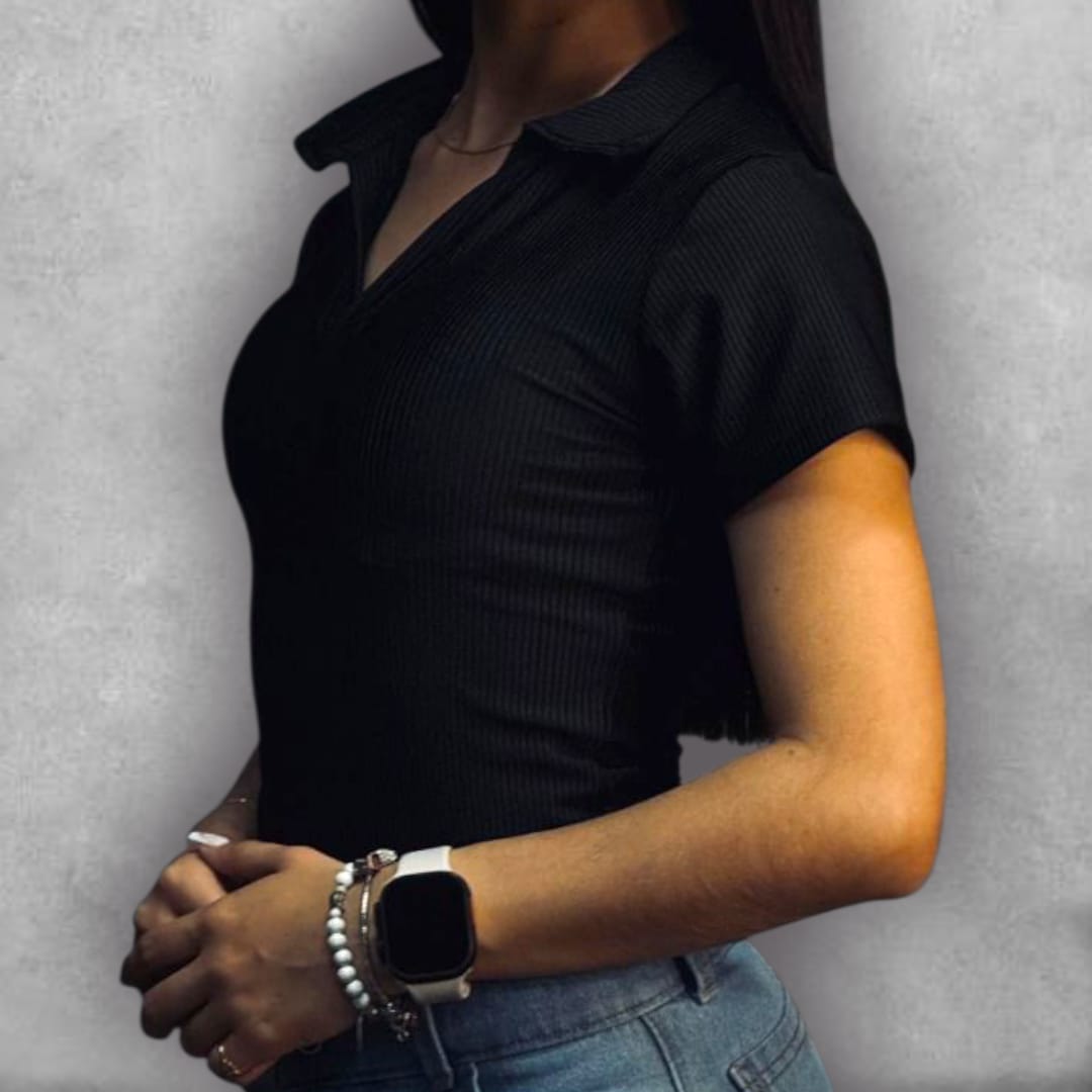 Añade un toque sofisticado a tus básicos con el Body Clamford – Ribbed Polo Edition. Su construcción acanalada en negro intenso ofrece una textura rica y un confort excepcional. El detalle del cuello tipo polo con escote en V le da un giro chic al diseño de manga corta. Esta pieza ajustada es esencial para lograr una silueta limpia bajo cualquier prenda inferior, asegurando que tu estilo se mantenga impecable en cualquier ocasión.